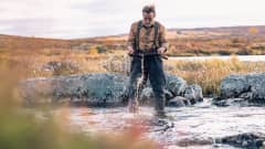 En ensam man vaskar efter guld stående i en fjällbäck. 