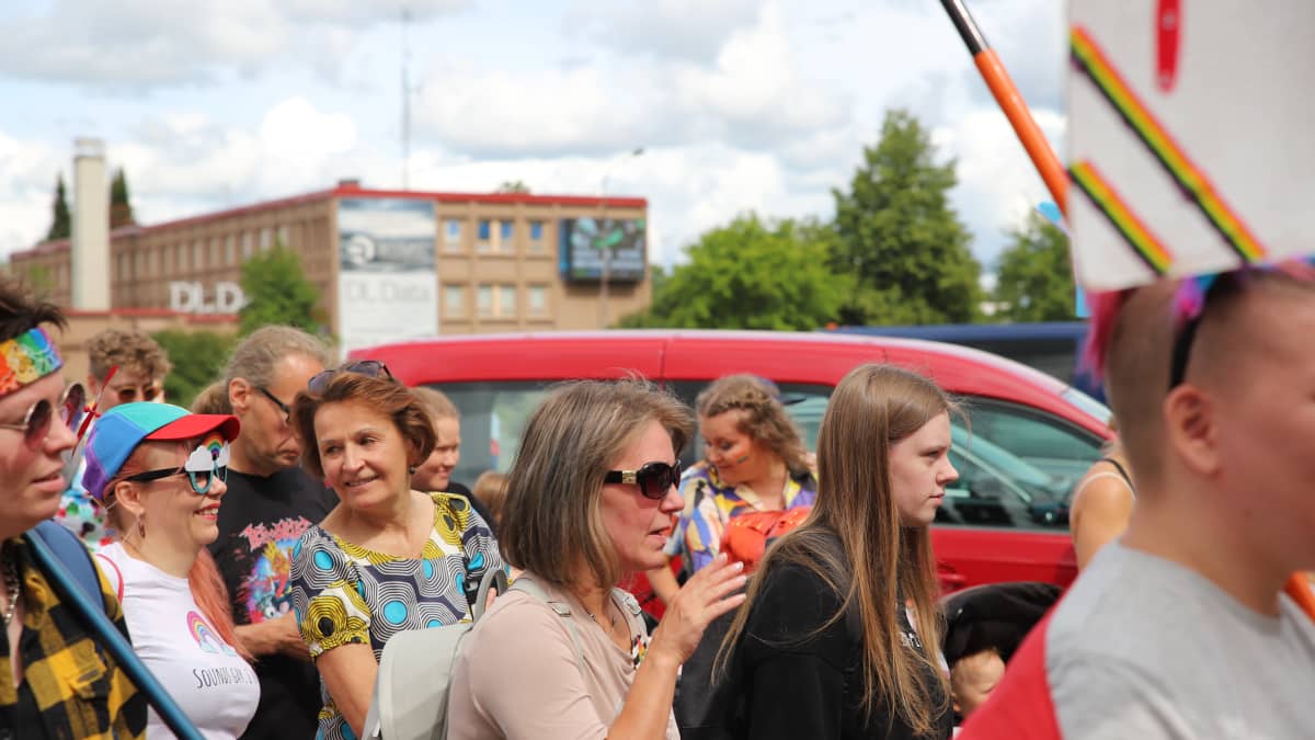 Pride-tapahtumassa liikkuvia ihmisiä Lapualla aurinkoisena kesäisenä päivänä, kuvissa näkyy sateenkaarilippuja ja Anneli Jäätteenmäki.
