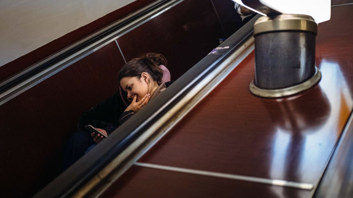 Nuori nainen istuu metron liukuportaissa selaamassa kännykkäänsä.