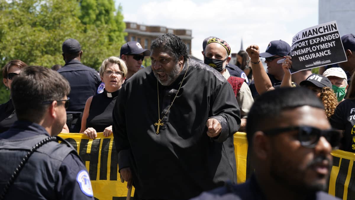 Hyvin lihava musta pastori risti kaulassa osallistuu mielenosoitukseen. 