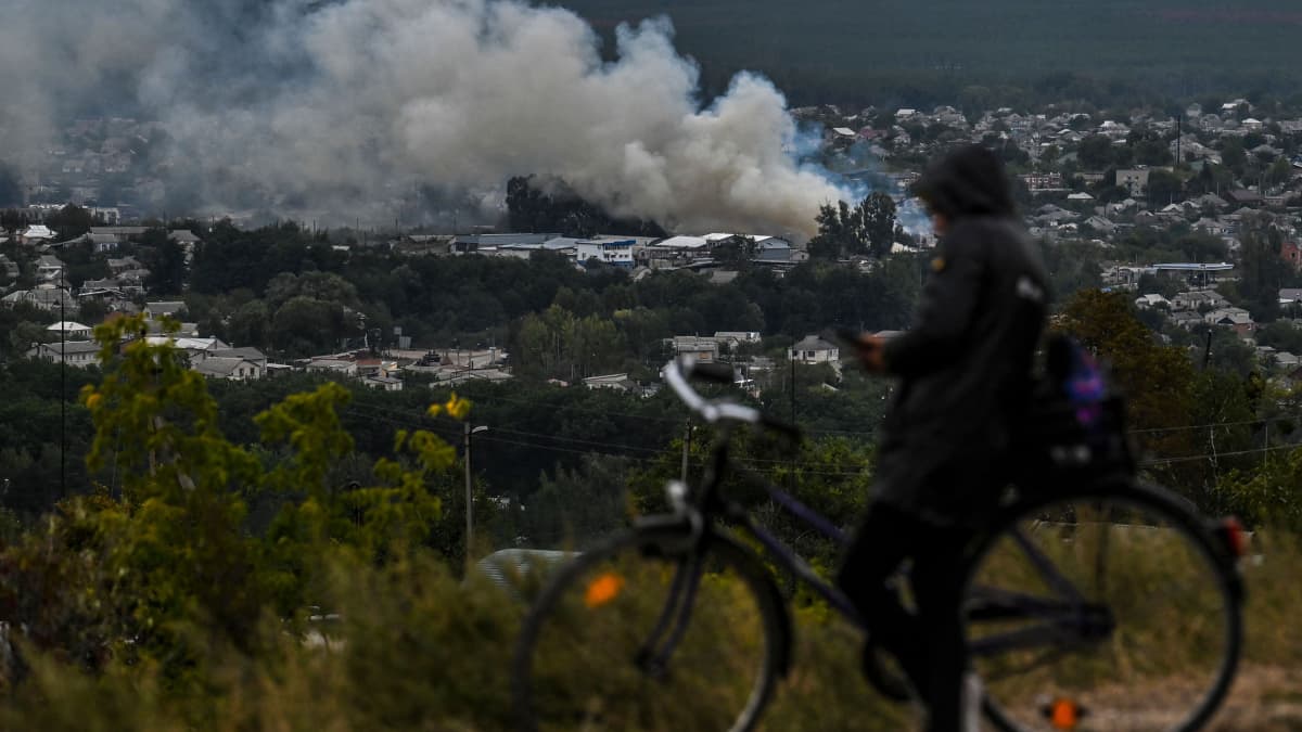 Pyöräilijä katselee savuavaa Iziumin kaupunkia.