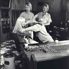 Abba-yhtyeen jäsenet ovat musiikkistudiossa. Björn Ulvaeus ja Benny Andersson seisovat. Agnetha Fältskog istuu miksauspöydän ääressä ja nauraa, kun Anni-Fris Lyngstad on painautumassa pää edellä hänen syliinsä.