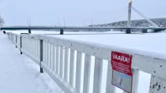 Etualalla puista aitaa, ja heikoista jäistä varottava kyltti. Taustalla Jätkänkynttilä-silta.