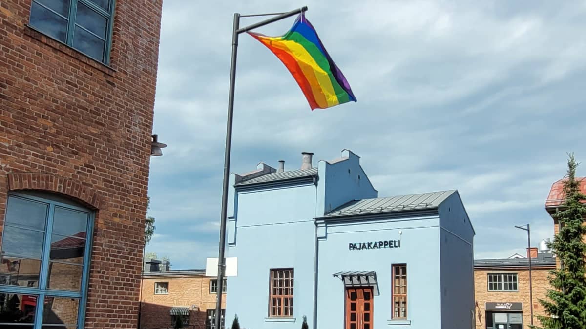 Sateenkaarilippu liehuu Lapuan Vanhan Paukun pihalla, taustalla näkyy sininen rakennus jossa lukee Pajakappeli.