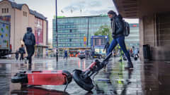 An e-scooter lying on the pavement in Helsinki's Elielinaukio as pedestrians pass by. 
