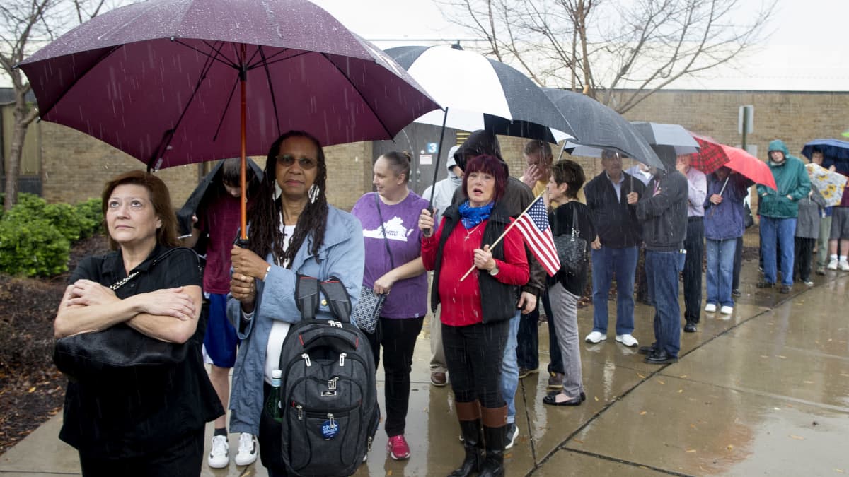 Joukko ihmisiä jonottaa rankkasateessa äänestämään Virginiassa vuonna 2018. Monilla on suuri sateenvarjo. 