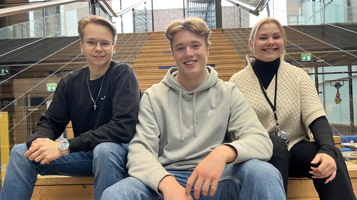 Kolme opiskelijaa istuu portailla hymyillen.