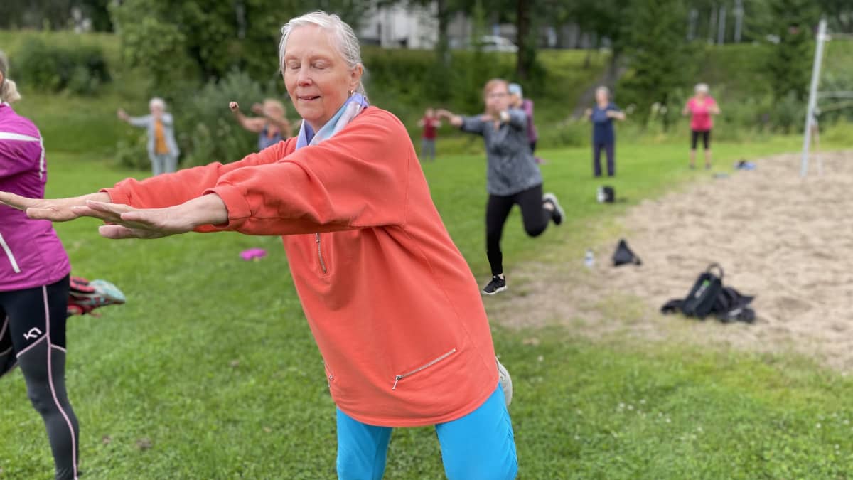 Vanhempi nainen jumppaa yhdessä muiden kanssa puistossa. 