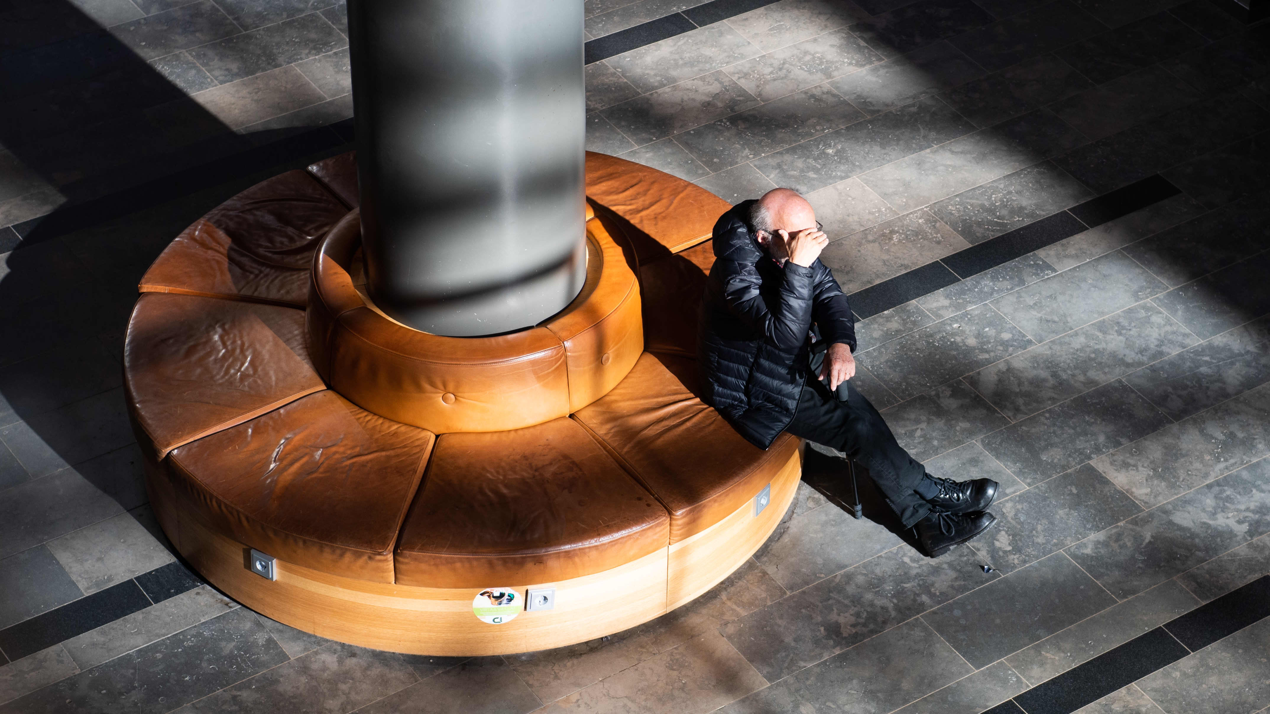 Eläkeikäinen mies istuu penkillä kauppakeskuksessa Espoossa.