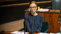 Woman with brown hair and eyeglasses, wearing a blue shirt sitting at a desk in parliament, looking into the camera.