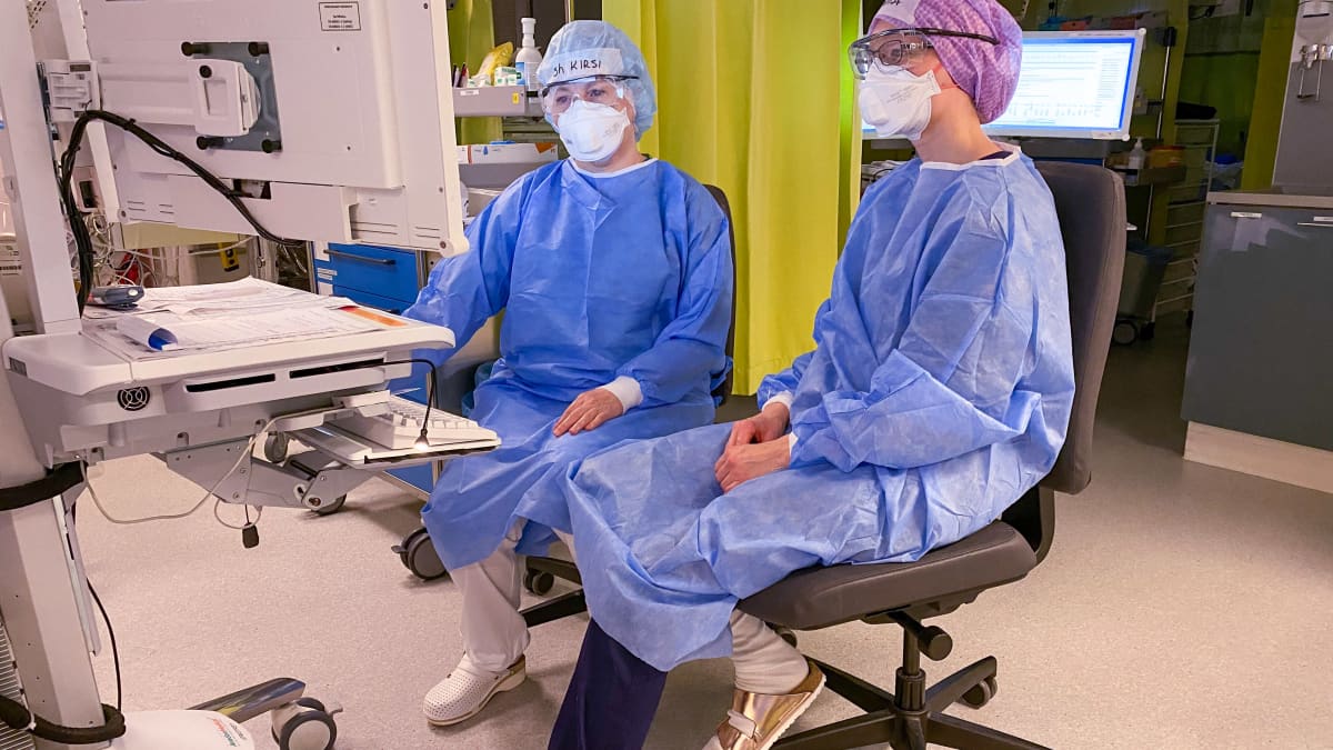 Kaksi sairaanhoitajaa sinisissä suoja-asuissa monitorien ääressä sairaalan teho-osastolla.