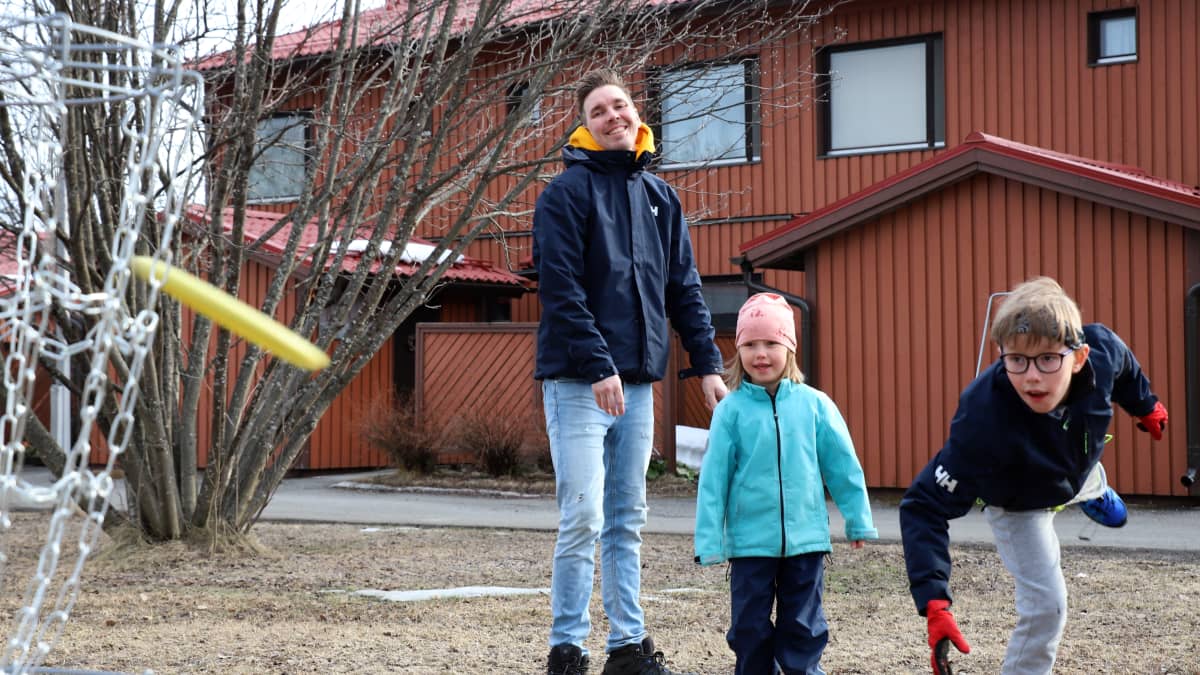 Poika (Elmo Hyöppinen) heittää frisbeen koriin, vieressä sisko Mila ja isä Kimmo Hyöppinen.