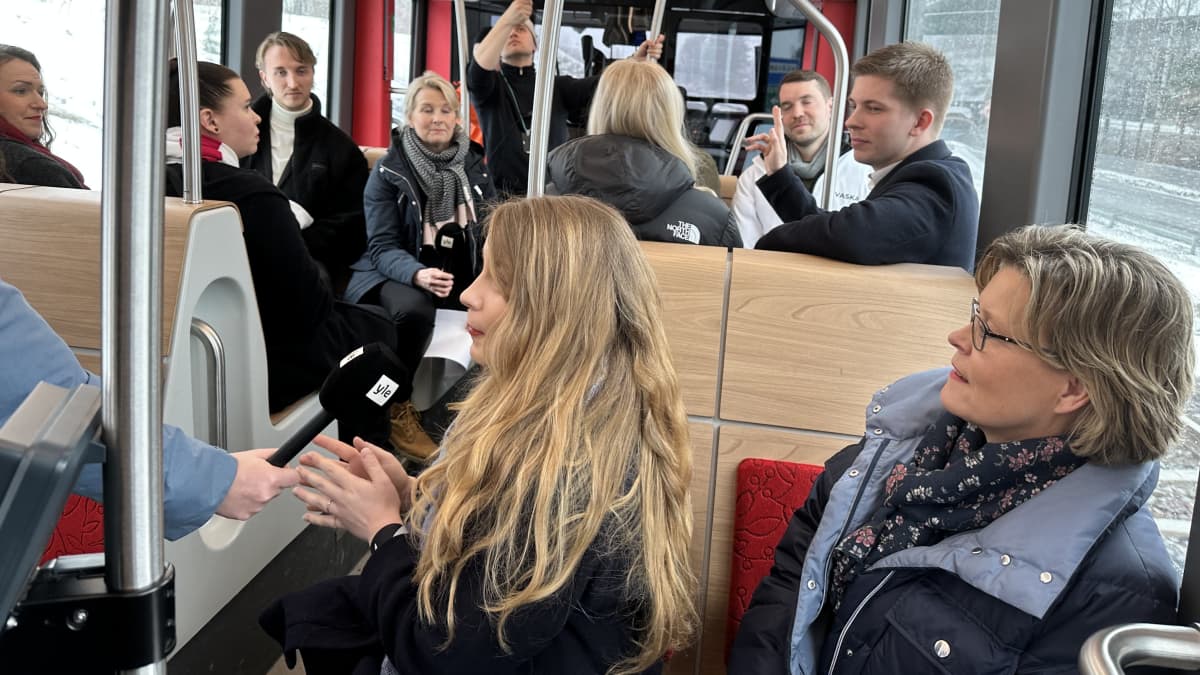 Iiris Suomela vastaa hänelle ojennettuun mikrofoniin. Hänen takanaan istuu Sari Tanus. Taustalla näkyy lisää Ylen ratikkatenttiin osallistuvia ehdokkaita.
