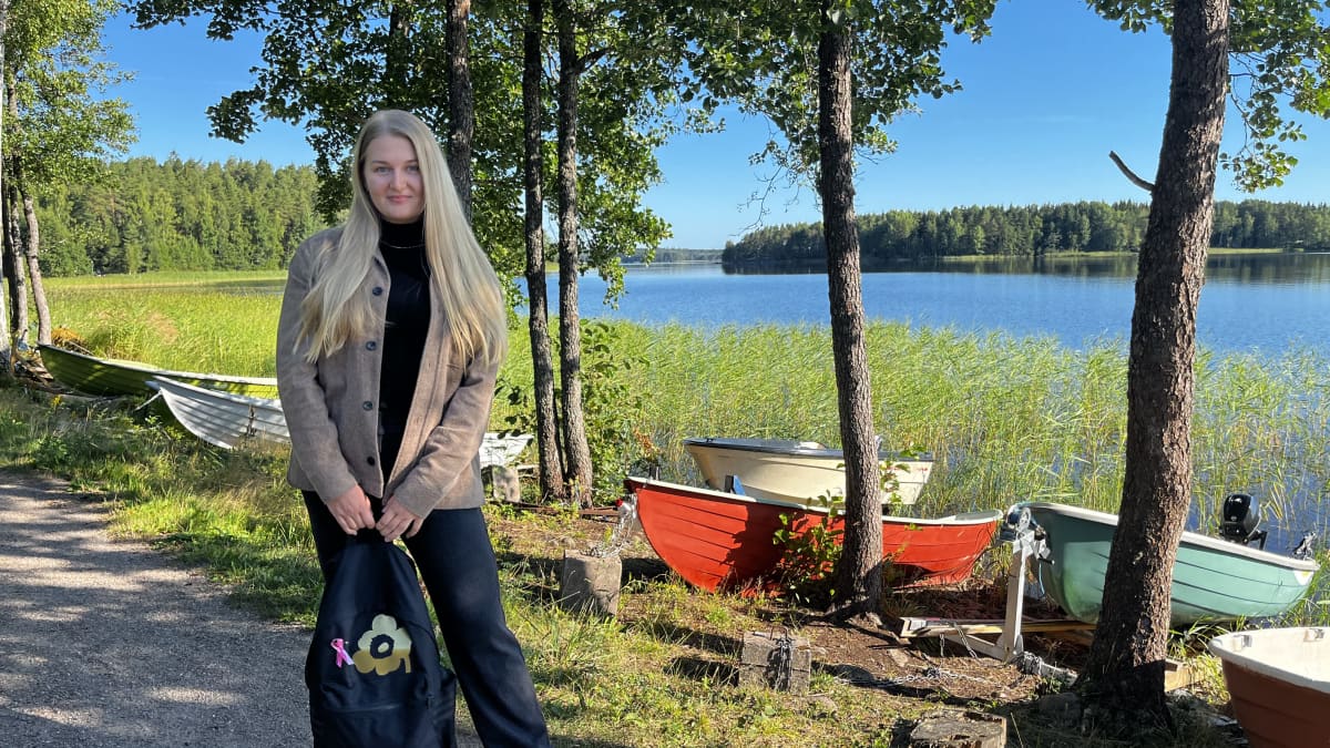 Nuori nainen marimekko-repun kanssa. Taustalla Saimaa, rantojen vihreät metsät ja soutuveneitä.