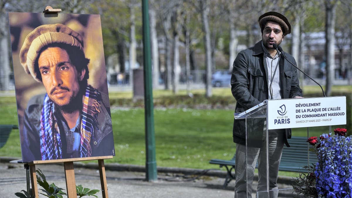 Ahmad Massoud puhuu puistossa puhujanpöntön takana, päässään perinteinen päähine, Vieressä on maalaus hänen isästään.
