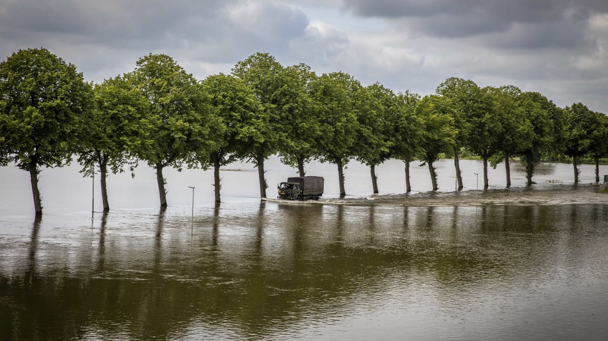 Kuorma-auto ajaa puiden reunustamaa ja veden peittämää tietä.