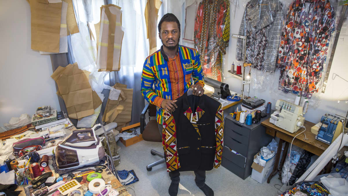 Dennis Owusu seisoo työhuoneessaan ja pitää suunnittelemaansa paitaa kädessä
