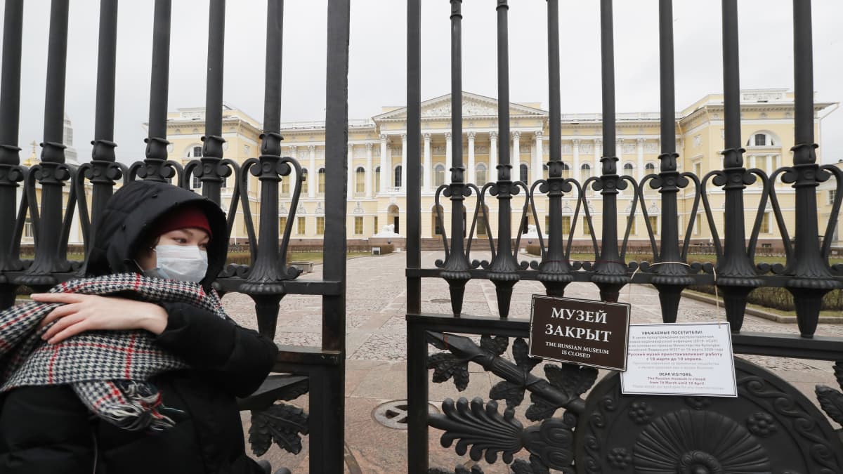 Hengityssuojaa käyttävä nainen kulkee Pietarissa suljetun Venäläisen taiteen museon portin ohitse.