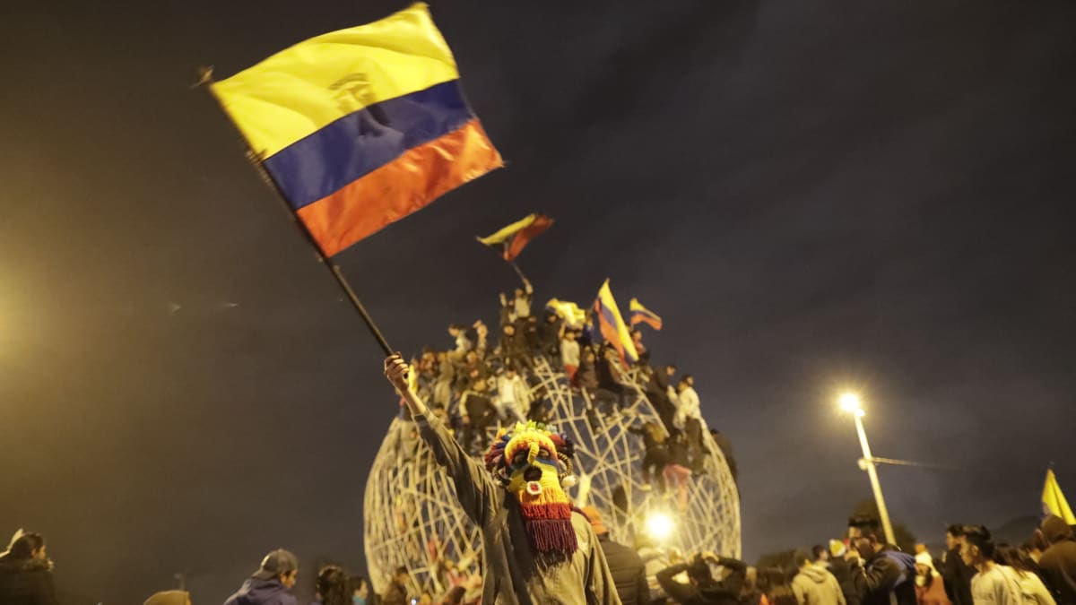 Värikkäällä naamiolla naamioitunut ihminen heiluttaa Ecuadorin lippua.
