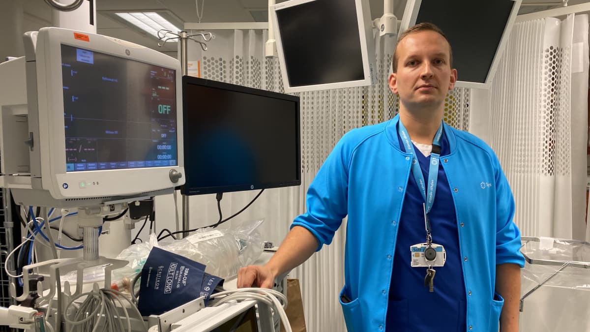 Ylilääkäri Mikko Franssila katsoo kameraan. Hänen ympärillään on erilaisia sairaalaympäristöön kuuluvia näyttöjä.