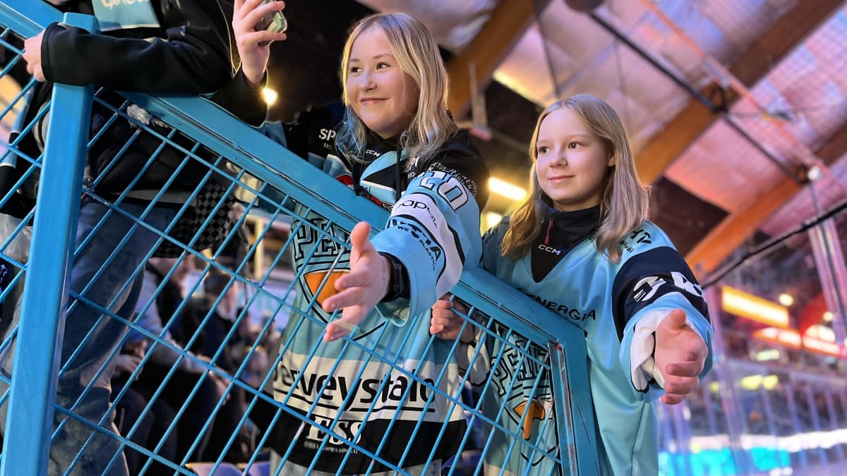 Helinä Heikkilä ja ViiviTähtinen aidan vieressä, kädet ojossa ja kännykät kädessä Pelicans-paidat päällä.