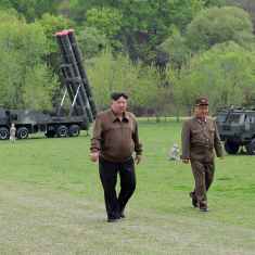 Kim Jong-un ja kaksi sotilashenkilöä kävelee nurmikentällä. Taustalla ohjusjärjestelmiä.
