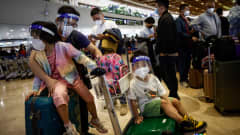 Maskeihin ja visiireihin pukeutunut kiinalainen perhe lentoaseman check-in jonossa. 