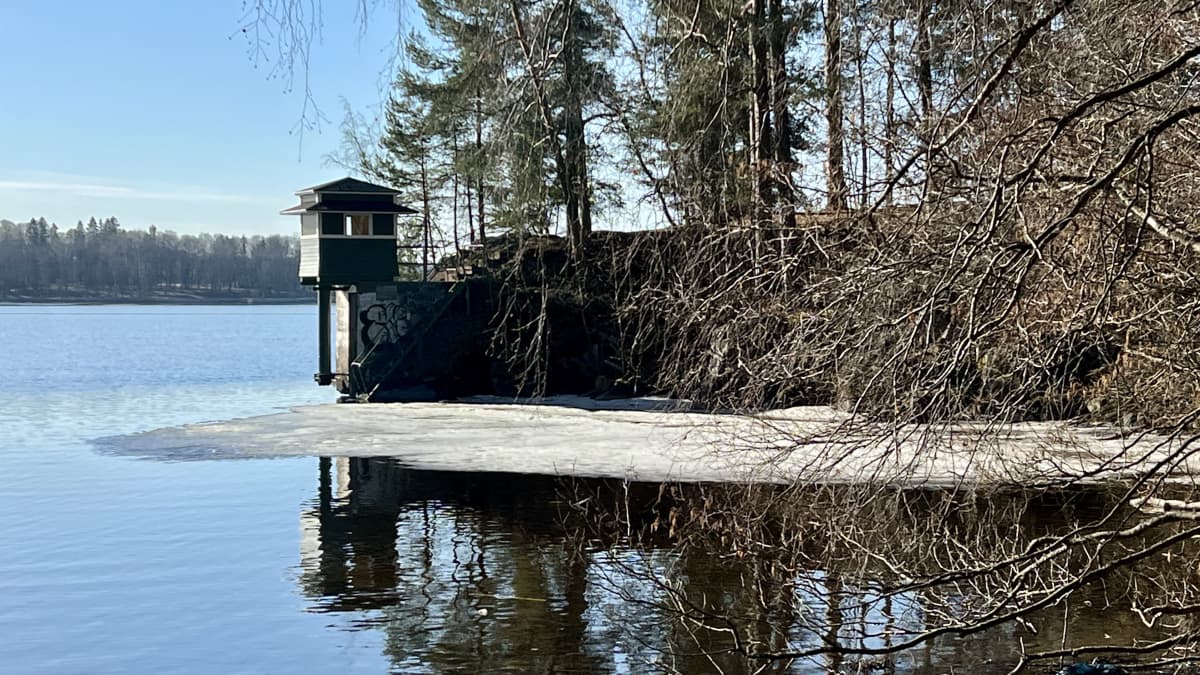 Niemen nokassa on pieni vihreäksi maalattu rakennus. Rakennuksen edessä vedessä on muutama jäälautta.