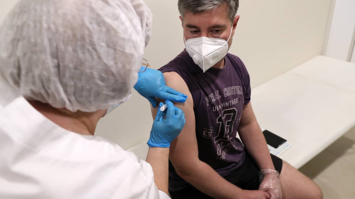 Hoitaja rokottaa maskiin pukeutunutta miestä