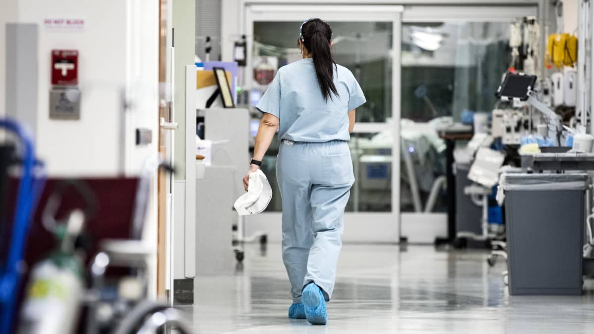 En sjukskötare går i en sjukhuskorridor. Hon har ryggen mot kameran.