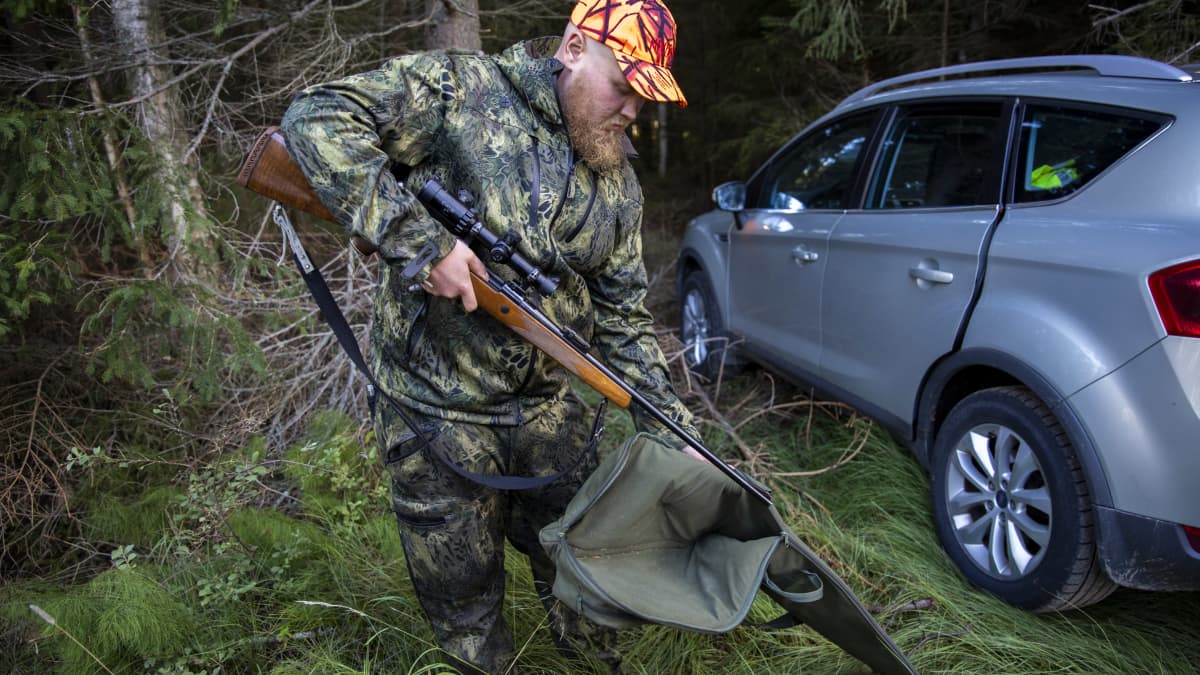 Metsästäjä Miro Oikarinen laittaa kivääriään suojapussiin autonsa vierellä metsässä.