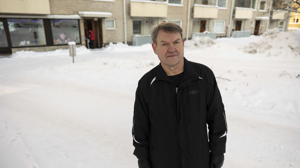 Taloyhtiön puheenjohtaja Yrjö Ojala seisoo talon etupihalla. Taka-alalla luminen piha ja kerrostalon alimmat kerrokset. 