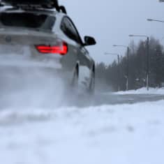 Auto ajaa talvisella tiellä, lumi pöllyää.