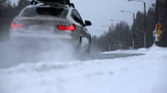 Auto ajaa talvisella tiellä, lumi pöllyää.