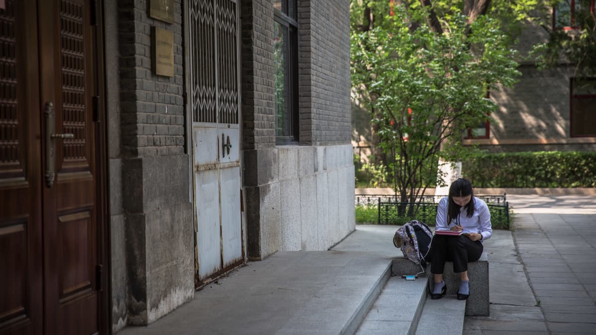nuori nainen istuu yliopiston porrastasanteella ja lukee kirjaa