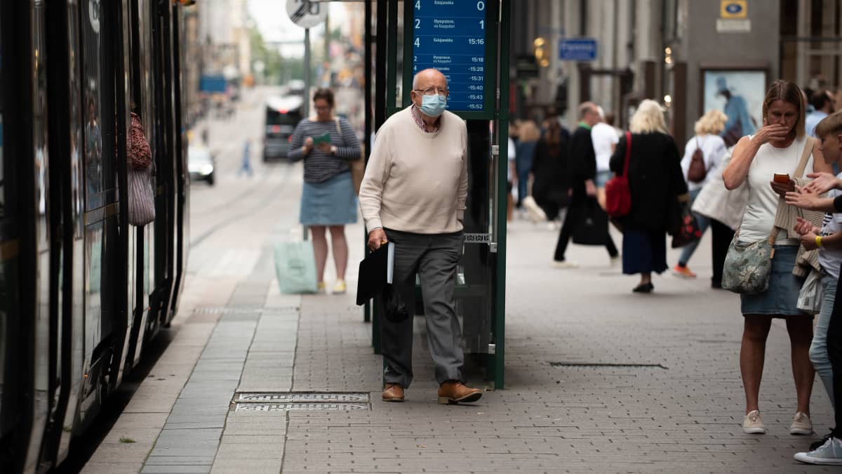 Vanha mies kävelee raitiovaunusta ulos raitiovaunusta kasvomaski päässään.