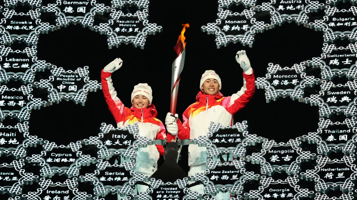 Kaksi ihmistä pitää olympiasoihtua ja vilkuttaa.