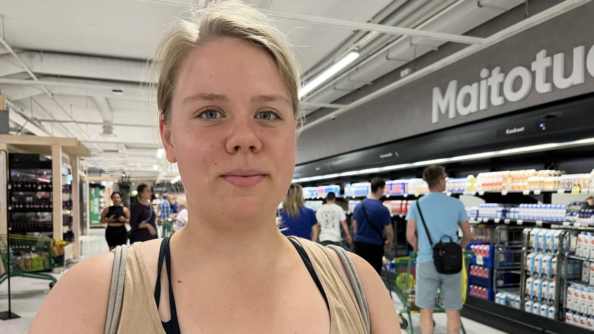 Kristiina Lehtimäki hymyilee kuvassa Prisman maitotiski ja muita asiakkaita taustallaan.