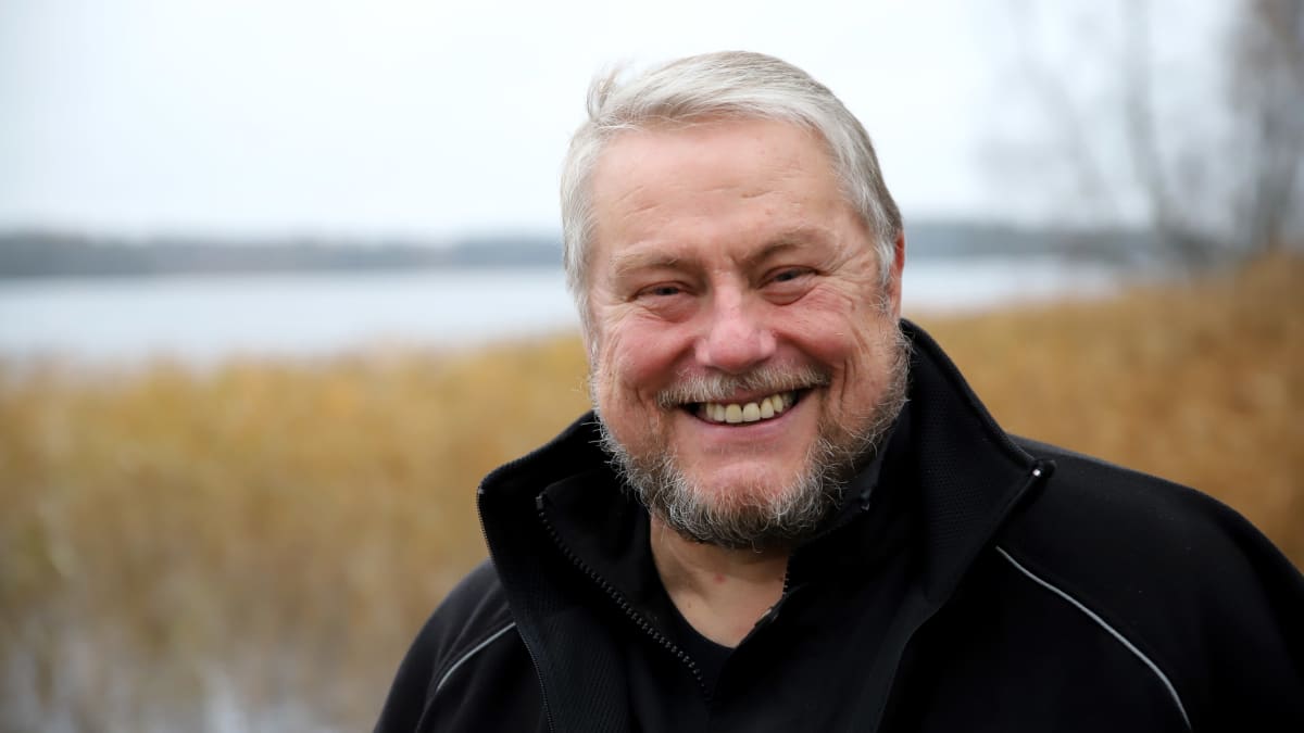 Tuomas Koskinen hymyilee kameralle, järvi taustalla.