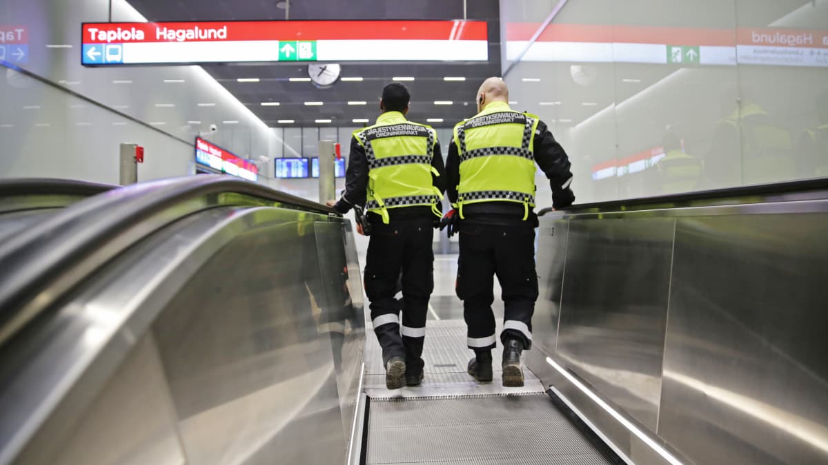 Kaksi vartijaa metroaseman liukuportaissa.