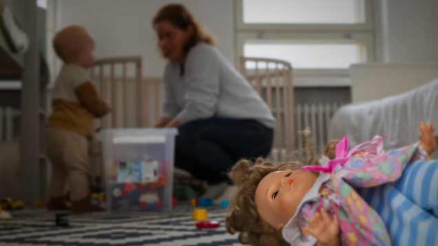 Lapsi ja aikuinen leikkivät taustalla ja kuvan etualalla makaa nukke.