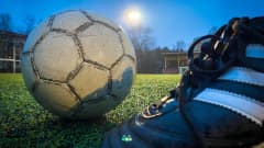 Jalkapallokenkä ja jalkapallo kuvattuna Pyynikin tekonurmikentällä. Takana kajastaa kentän valonheittimen valo.