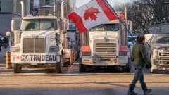 Två långtradare blockerar en gata. Framför dem går en man med Kanadas flagga. Flaggan hänger år fel håll