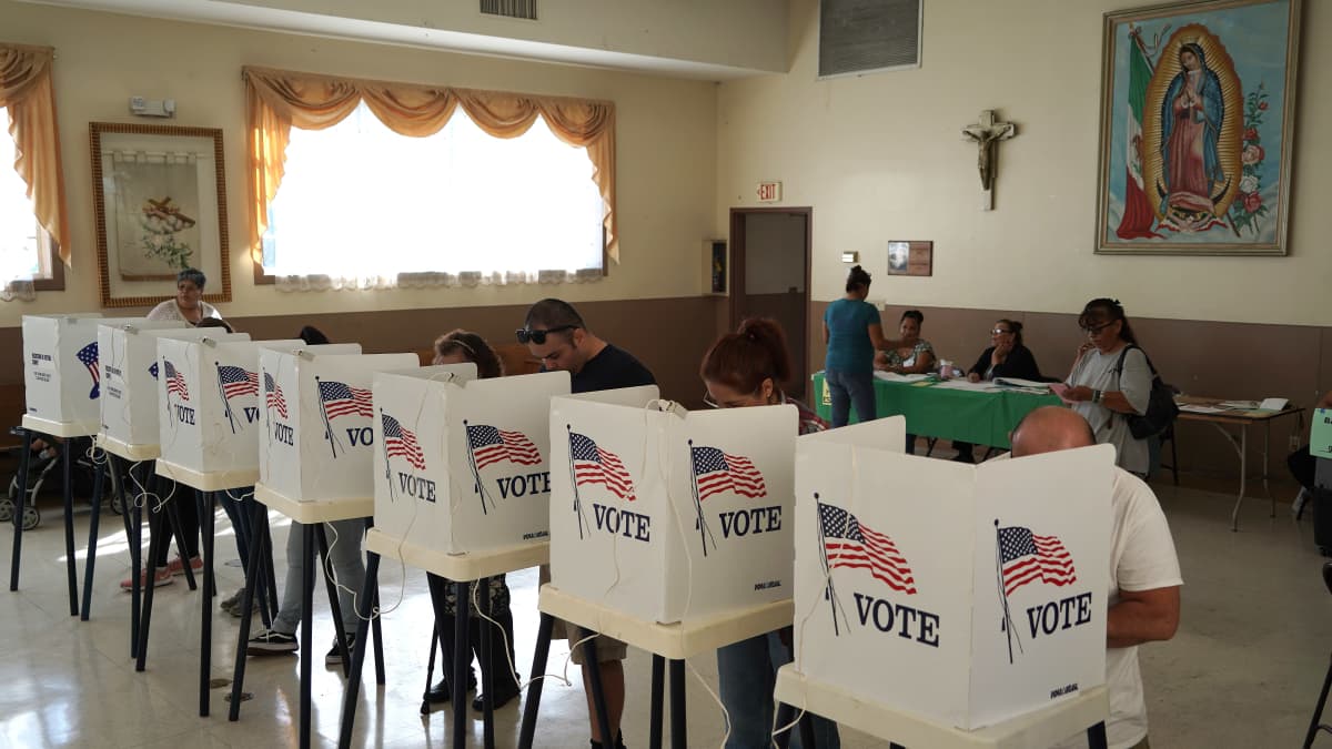 Joukko äänestäjiä äänestykopeissa Los Angelesissa vuonna 2018. Valkoisissa kopeissa on Yhdysvaltain lippu ja  lukee englanniksi Vote.