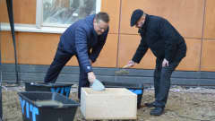 Kaksi miestä laittaa laastia puulaatikkoon. 