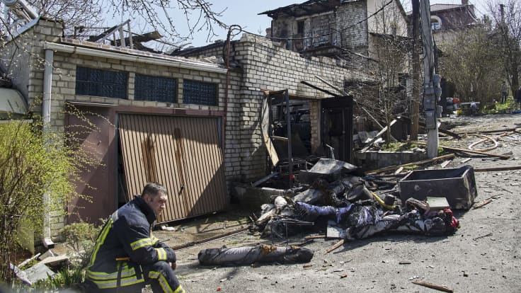 Pelastustyöntekijä istuu vaurioituneen rakennuksen edessä.