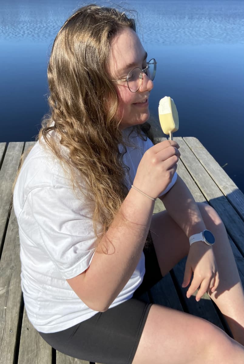 Kuvassa Hakalahden koulun oppilas istuu laiturilla ja syö jäätelöä.