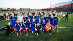 Gilla FC:n pelaajat kasassa poseeraamassa kameralle. Pelaajien takana on fanijoukko. 