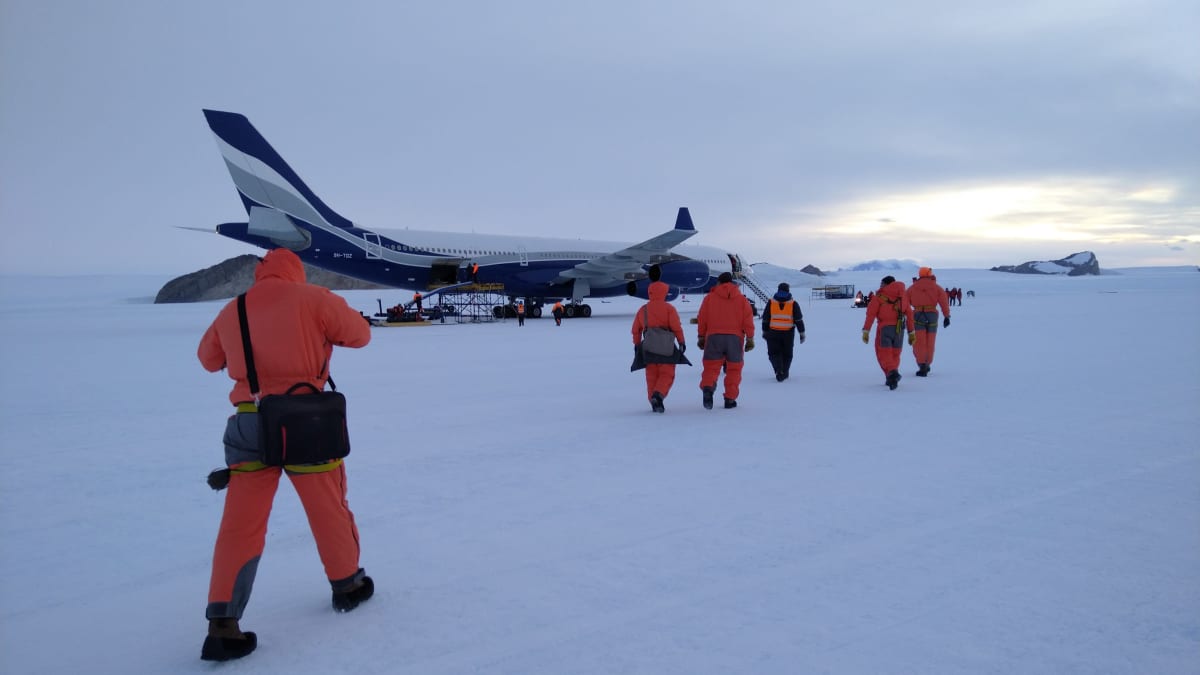 Ihmimset kävelevät kohti lentokonetta lumisessa maisemassa.