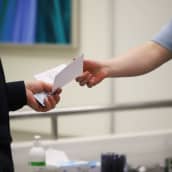 Aluevaalien toimitsija ojentamassa äänestyslippua äänestäjälle Kouvolan kaupunginkirjastossa.